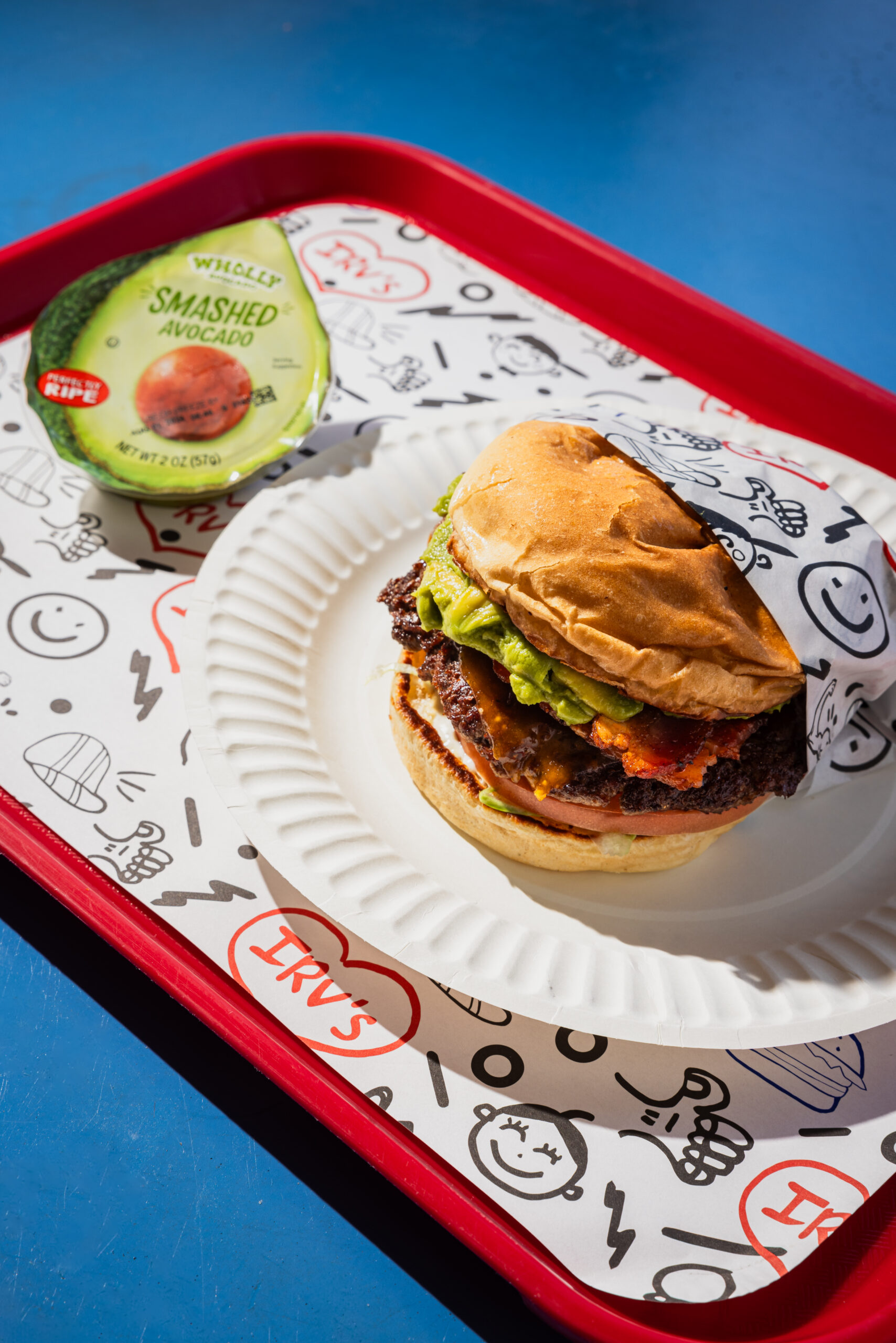 Wholly avocado bacon burger on a tray.